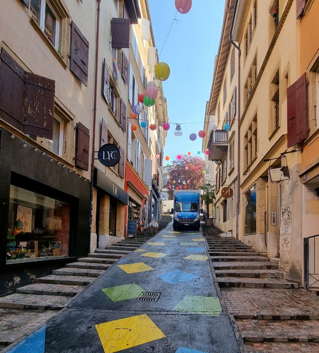 Blauer Transporter fährt eine Gasse mit Treppen und bunten Laternen hinauf